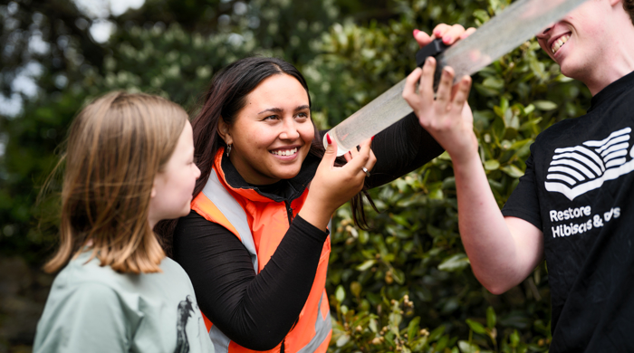 A young girl stands next to a woman holding a water clarity tube. A man stands to the other side, lifting the tube so the woman can see through it.