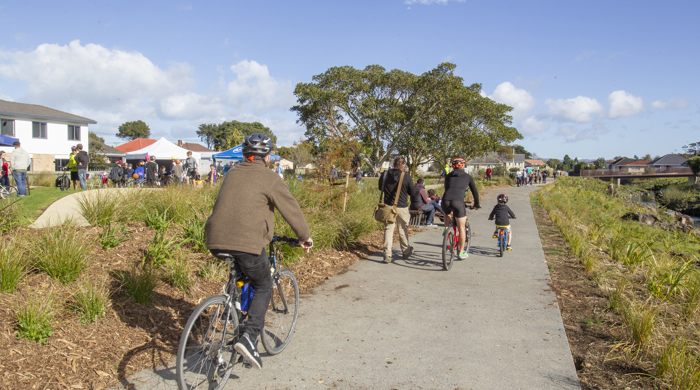 A family of adults and young children on bikes are cycling the new pathway between urban houses and the waterway.