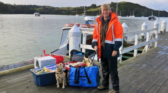 Rosie the biosecurity dog and Rochelle, Rosie’s handler, standing in front of a boat at Sandspit Wharf, checking for any pests in materials, before they are loaded to be taken to Kawau island.