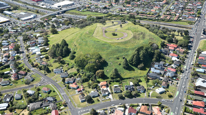 An aerial view of the mostly grassed maunga surrounded by houses and industry.