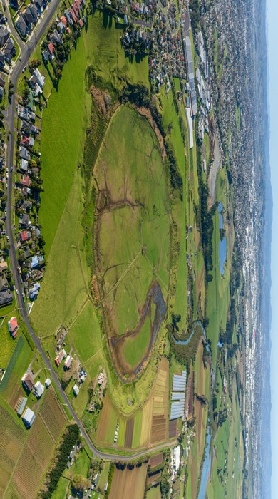 An aerial photo of a large grassy area surrounded by housing and farmland. A circle (the crater rim) is defined by vegetation.